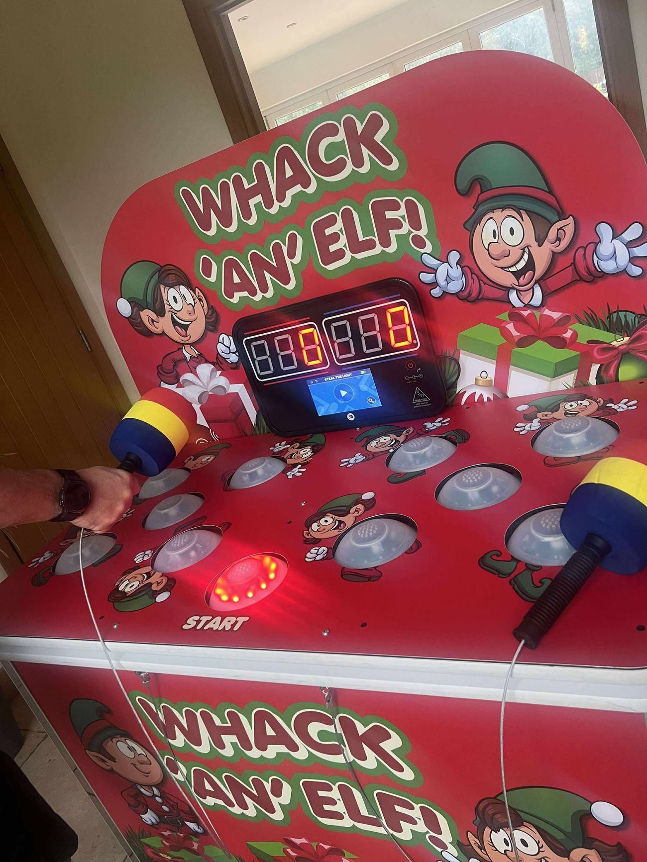 Player raising a padded mallet over the light-up dome buttons of the Whack an Elf game