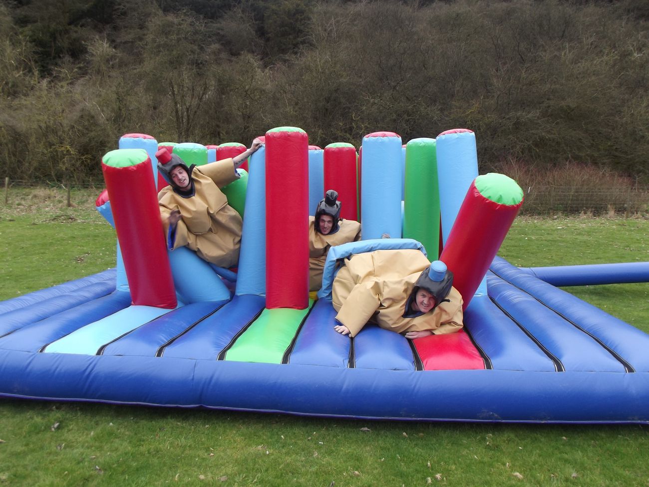 Three players in padded suits and helmets laughing as they scramble through the padded columns on the inflatable