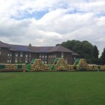 125ft army inflatable assault course inflated in a field in front of a block of flats