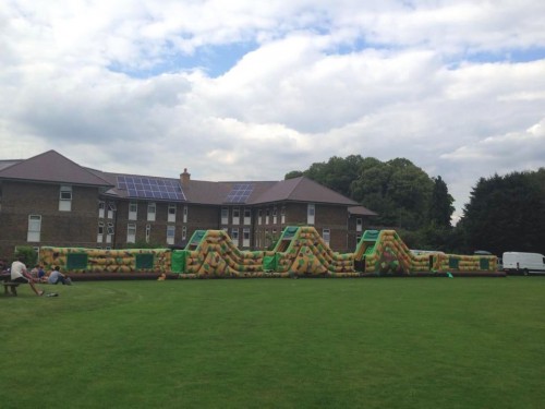 125ft army inflatable assault course inflated in a field in front of a block of flats