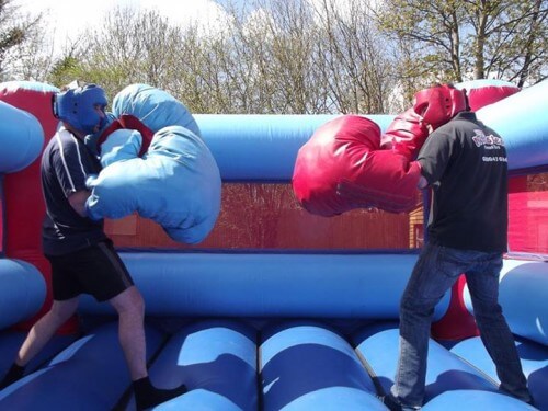 two boys geared up for a fight in a bouncy boxing inflatable with giant gloves and head guards